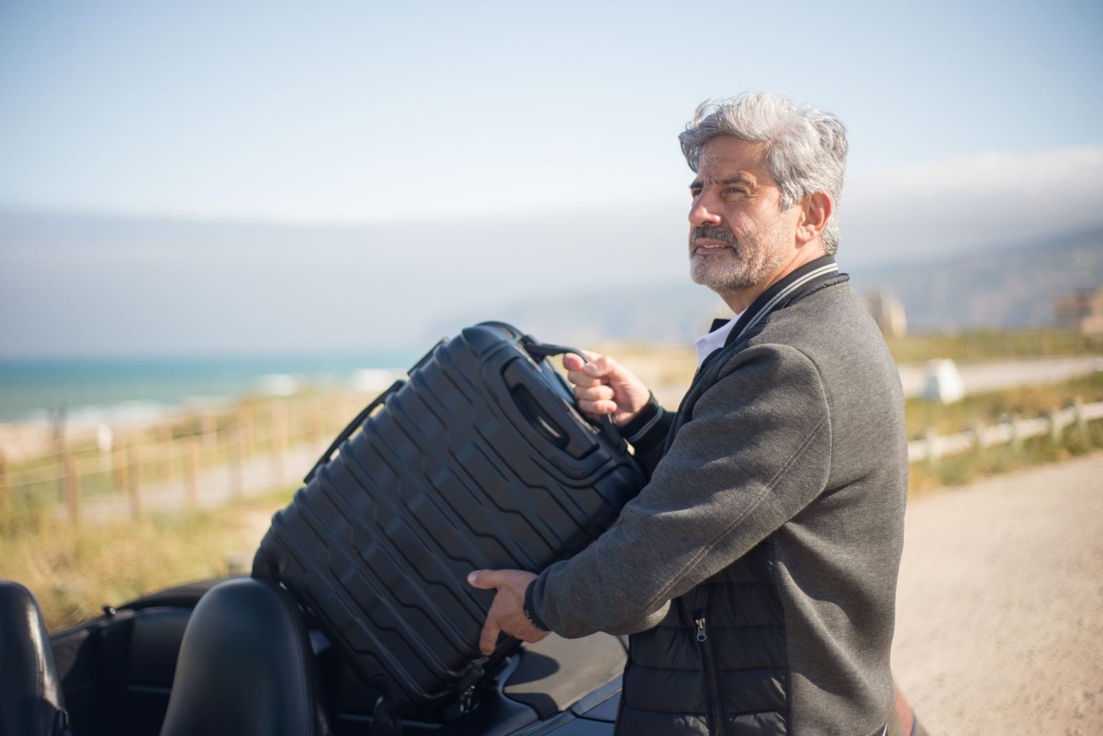 Man carrying a suitcase by the sea
